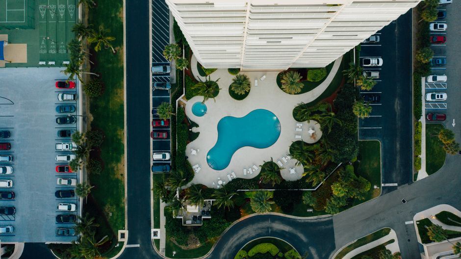 Top-down view of an apartment tower, pool, and open parking lots
